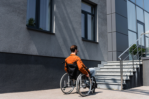 handicapped man in wheelchair near building with stairs on urban street