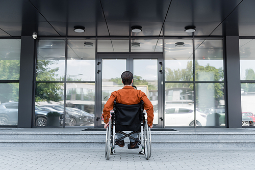 back view of handicapped man in wheelchair near stairs in front of building with glass facade
