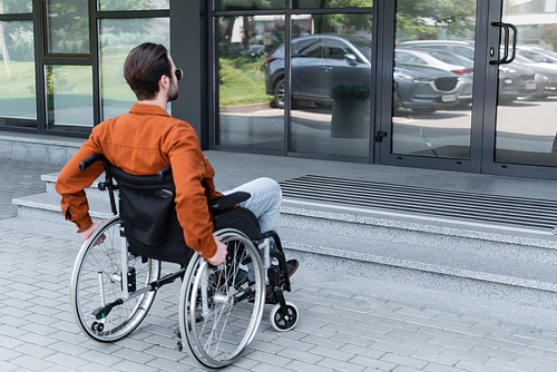 young disabled man in wheelchair near entrance of building with stairs
