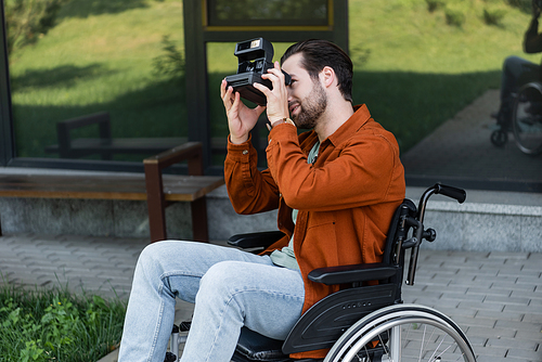 handicapped man in wheelchair taking picture on vintage camera outdoors