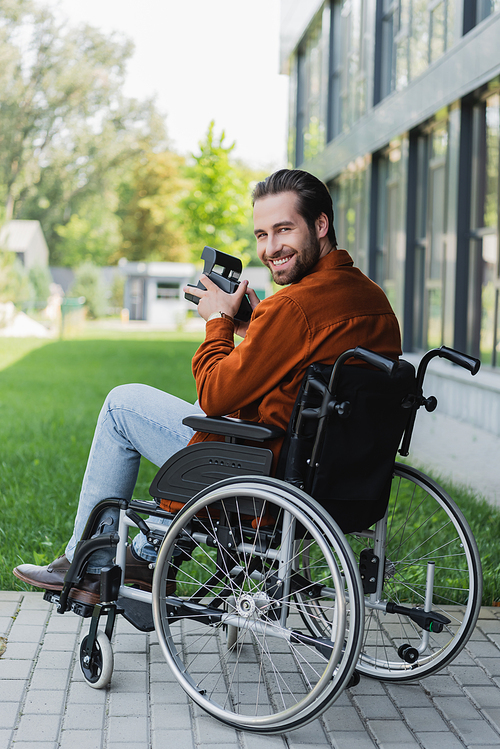 happy disabled man in wheelchair smiling at camera while holding vintage camera