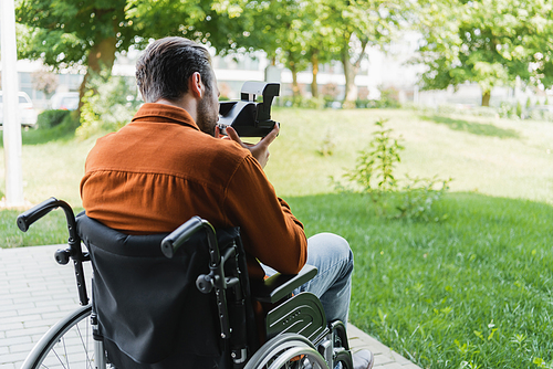 back view of handicapped man in wheelchair taking photo on vintage camera outdoors