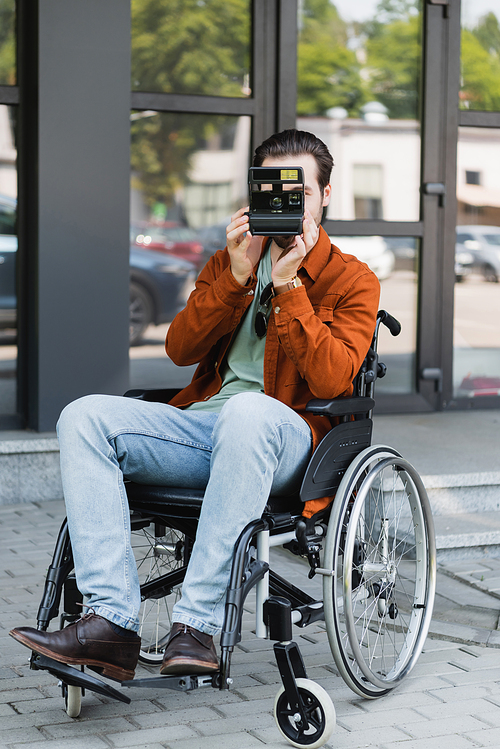 full length view of disabled man in wheelchair taking picture on vintage camera on street
