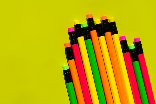 top view of colorful pencils with erasers on green background