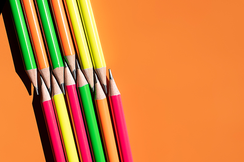 top view of colorful pencils on orange background