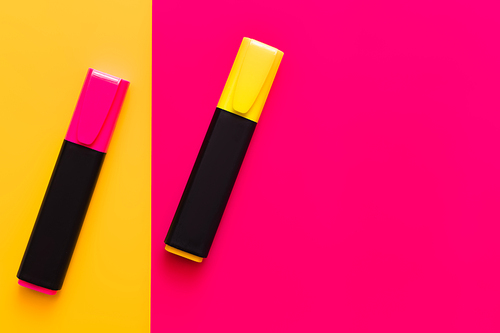 top view of colorful marker pens on pink and yellow background