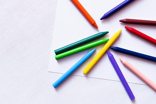 top view of colorful crayons on white paper and textured background