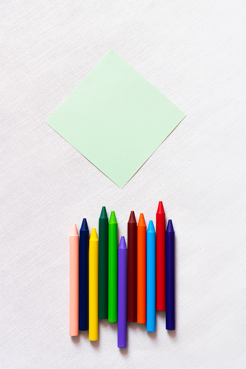 top view of colorful crayons near empty paper note on textured white background