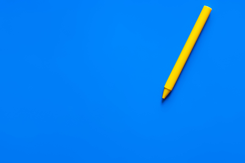 top view of yellow crayon on blue background