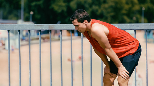 young sportsman breathing while resting after jogging on bridge