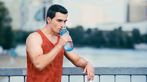 tired sportsman standing on bridge and drinking water from sports bottle