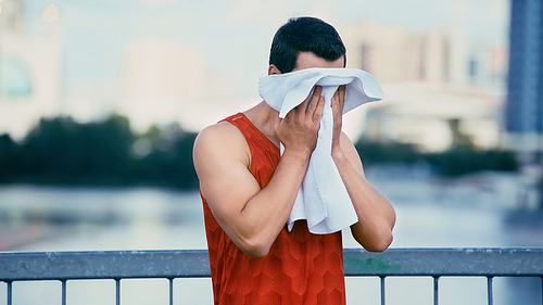 young sportsman wiping face with towel while standing on bridge