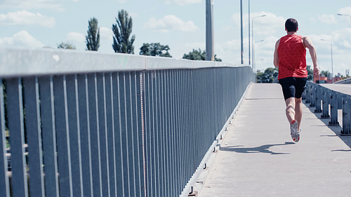 back view of young sportsman running on urban bridge in summer