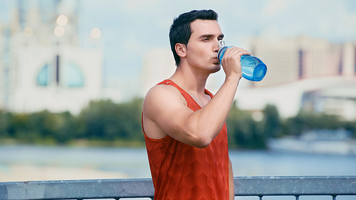 young sportsman standing on bridge and drinking water from sports bottle