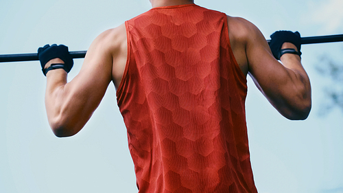 cropped view of young sportsman doing pull ups on horizontal bar outside