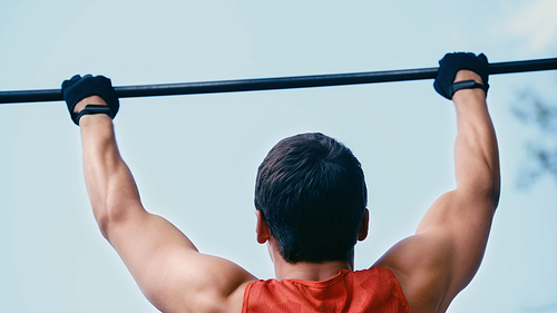 back view of young sportsman doing pull ups on horizontal bar outside