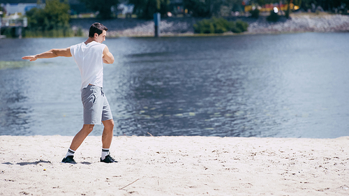 young sportsman in tank top and shorts doing body rotation near river