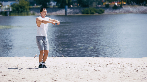 young sportsman in tank top and shorts warming up hands near river