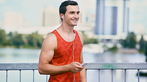 happy sportsman holding smartphone and listening music in earphones