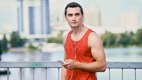 young sportsman holding smartphone and listening music in earphones