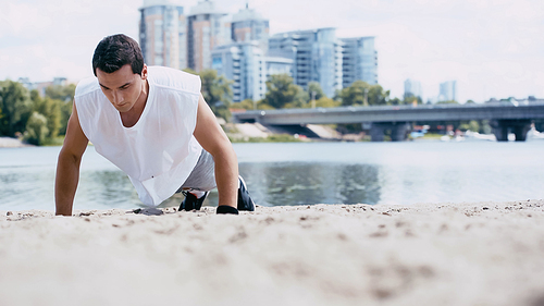 young sportsman doing push ups on sand near river