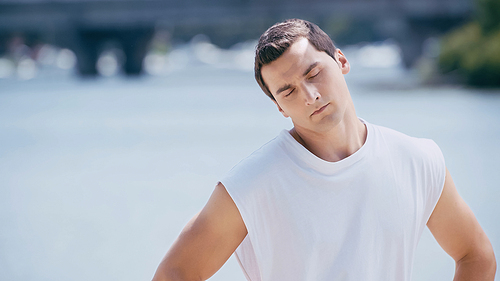 sportsman in tank top doing neck exercise near river