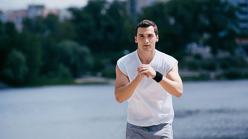 young sportsman in tank top working out near river