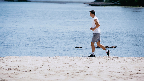 side view of young sportsman in tank top jogging near river