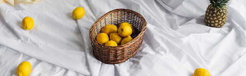 high angle view of ripe lemons in wicker basket near pineapple on white bed sheets, banner