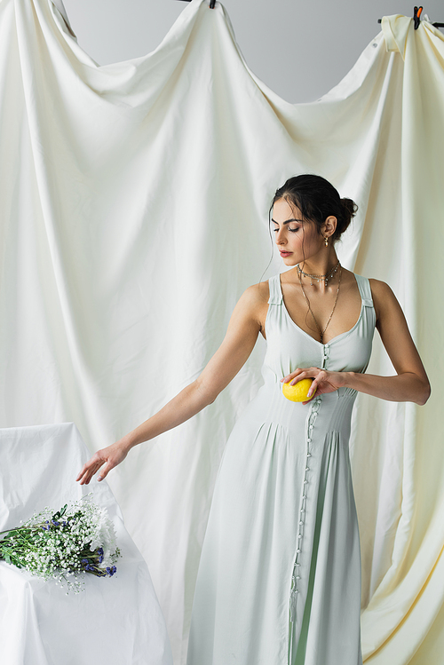 pretty woman reaching flowers while holding fresh lemon on white