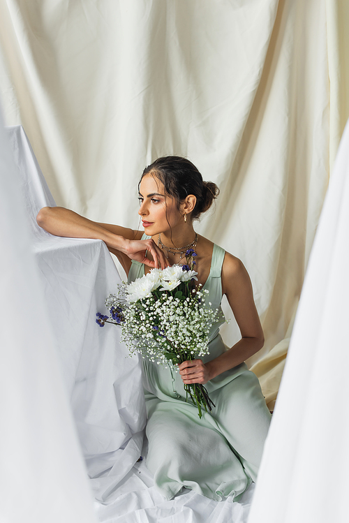 dreamy and pretty woman looking away while holding flowers on white