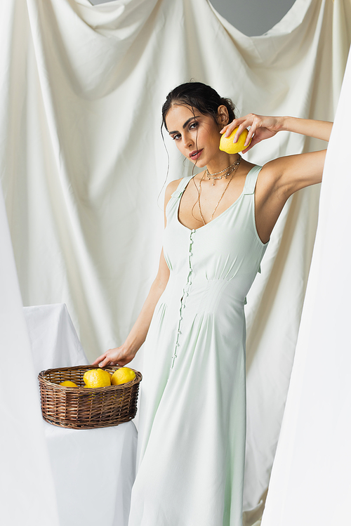 pretty woman in dress holding ripe lemon near wicker basket on white