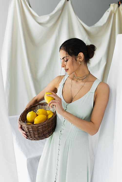 woman in dress holding ripe lemons in wicker basket on white