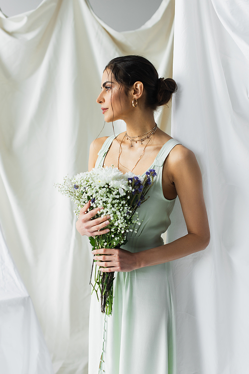 brunette woman in dress holding bouquet of flowers on white