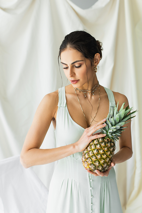 brunette woman in dress posing with pineapple on white