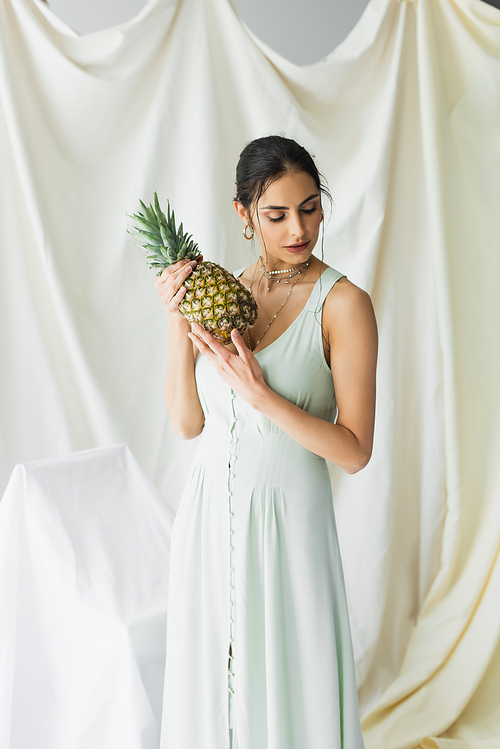 brunette woman in dress posing with ripe pineapple on white