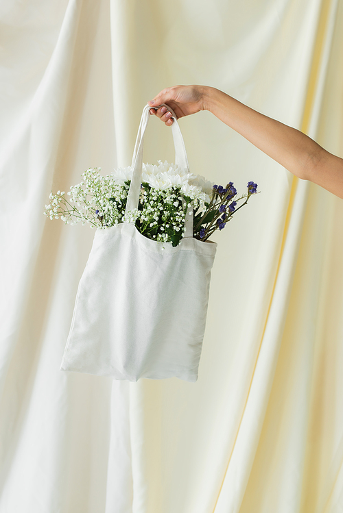 cropped view of woman holding fabric shopper bag with flowers on white