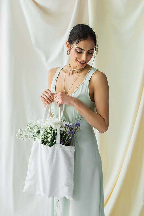 happy woman holding fabric shopper bag with flowers on white