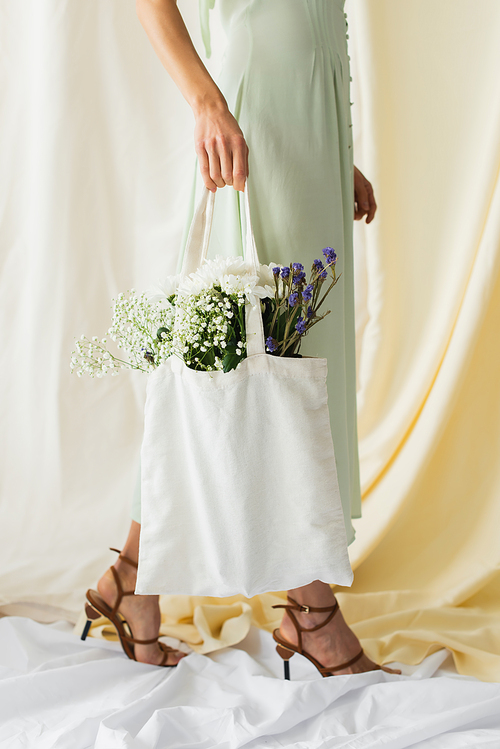 cropped view of woman holding fabric shopper bag with flowers and walking on white