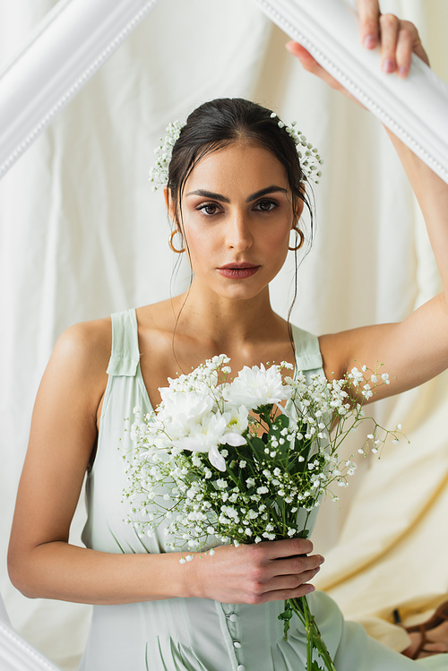 pretty woman holding bouquet of blooming flowers near frame on white