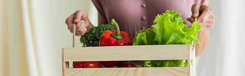 cropped view of woman holding wooden box with vegetables on white, banner