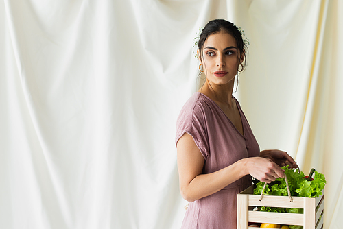 pretty woman holding wooden box with vegetables on white