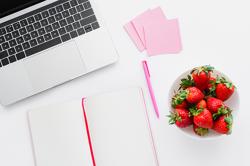 Top view of laptop near notebook and tasty strawberries on white background