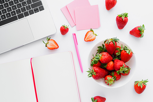 Top view of organic strawberries near laptop and notebook on white background