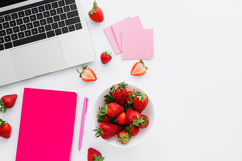 Top view of fresh strawberries near notebook and laptop on white background