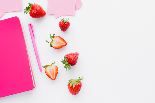 Top view of ripe strawberries near sticky notes and pink notebook on white background