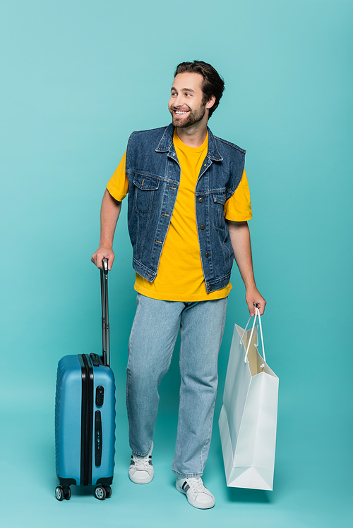 Smiling tourist with suitcase and shopping bag on blue background