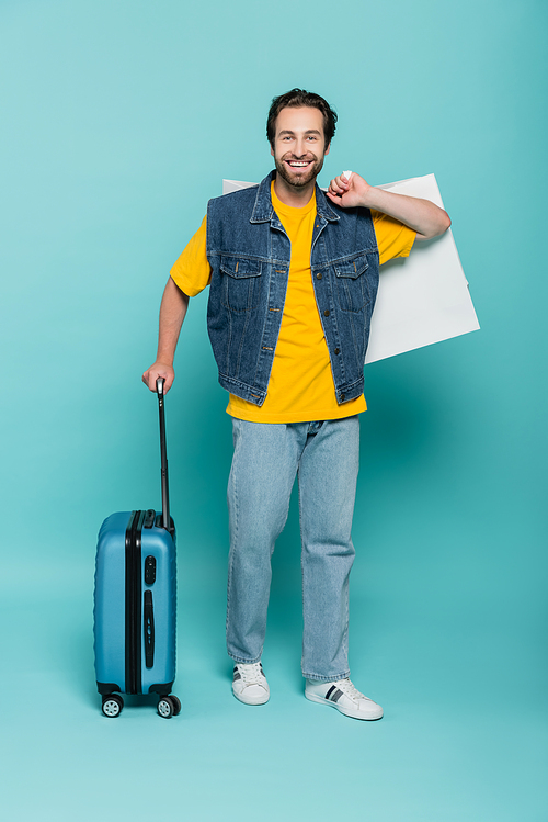 Positive man holding shopping bag and suitcase on blue background
