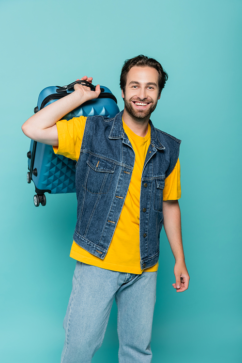 Cheerful tourist holding baggage isolated on blue