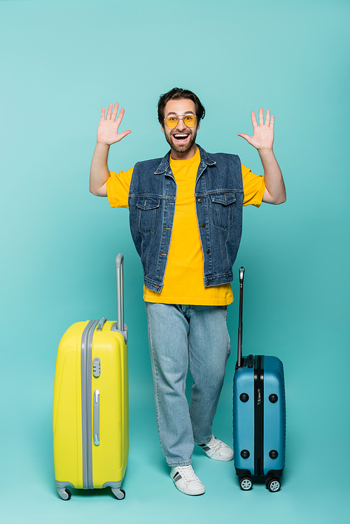 Happy traveler waving hands near suitcases on blue background
